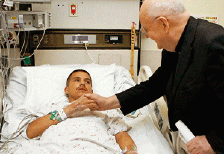 un sacerdote consuela a un joven que está enfermo en la cama del hospital