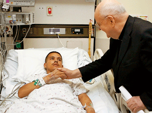 un sacerdote consuela a un joven que está enfermo en la cama del hospital