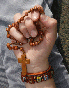 una mano sostiene un rosario con un crucifijo de madera