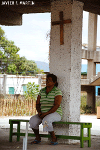 mujer en Venezuela sentada en un banco debajo de un crucifijo