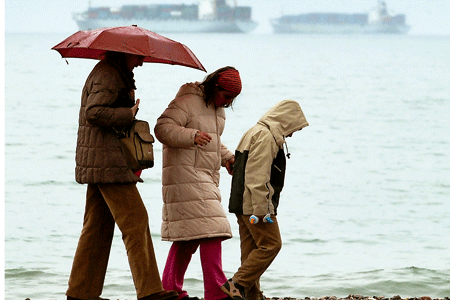 familia de una madre y dos hijos caminan bajo la lluvia
