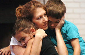 una madre abraza a dos hijos niño y niña