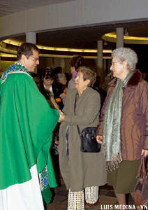sacerdote saluda a dos mujeres a la salida de misa