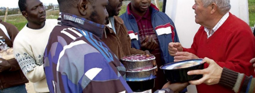 un hombre da tarteras con comida a un grupo de inmigrantes