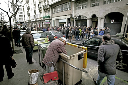 grupo de personas se manifiestan en la calle mientras un hombre busca en un contenedor
