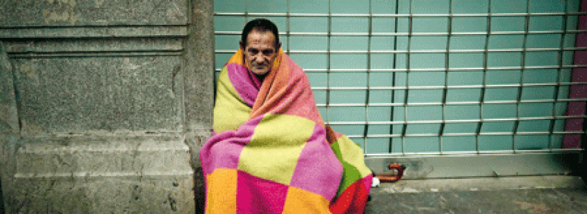Pobre en la calle arropado por una manta de colores