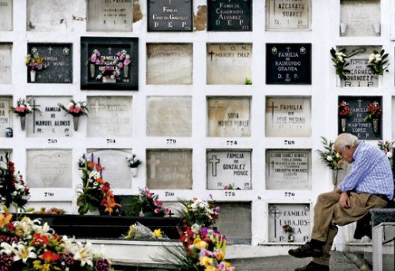 hombre mayor en un cementerio reza pensativo delante de las lápidas