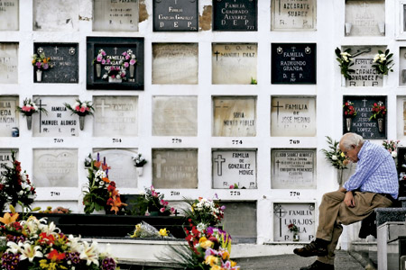 hombre mayor en un cementerio reza pensativo delante de las lápidas