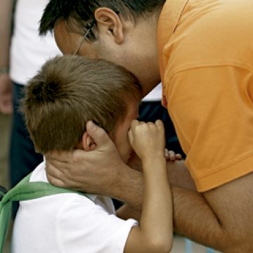padre besa a un hijo que está llorando al recogerlo del colegio
