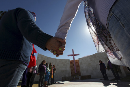 gente rezando cogida de la mano en círculo frente a una cruz