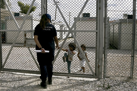 niñas iraquíes refugiadas hablando con una policía detrás de una valla en un centro de detención de inmigrantes en Grecia