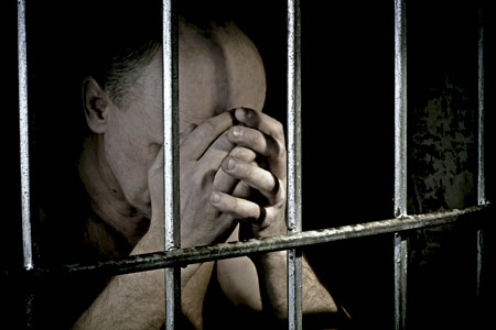 persona reclusa presa en una cárcel entre rejas rezando