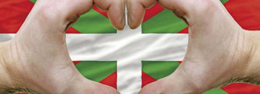 manos formando un corazón sobre una bandera del País Vasco