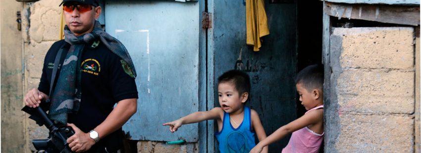 Un policía vigila vivienda en Filipinas durante operación antiidroga. Dos niños le observan