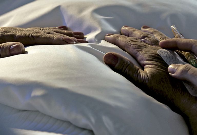 manos de mujer anciana en la cama con una enfermera que le pone una medicación