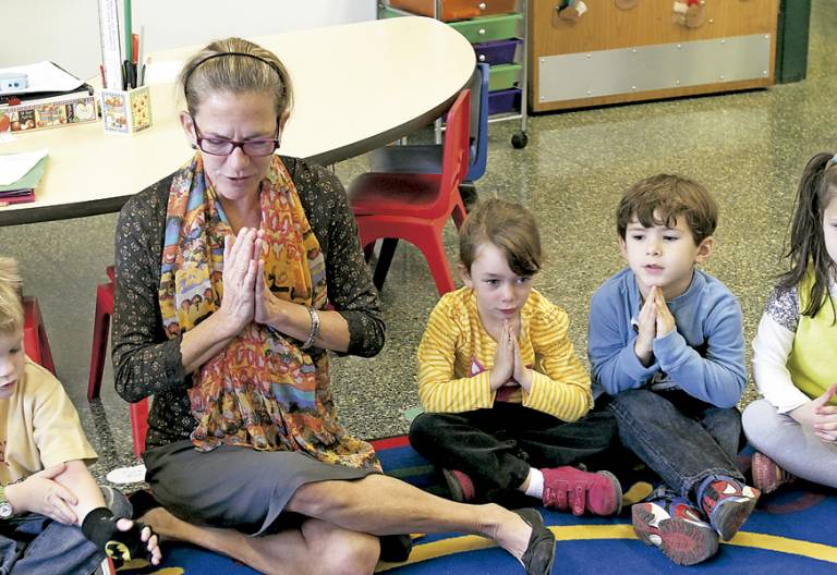 niños pequeños en el aula con la profesora rezando