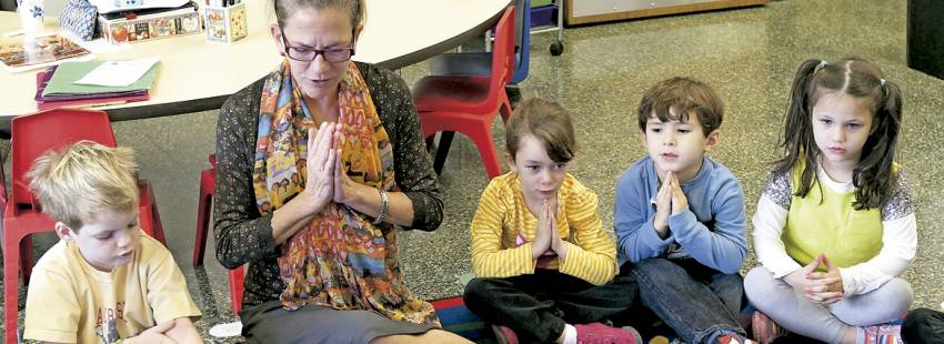 niños pequeños en el aula con la profesora rezando