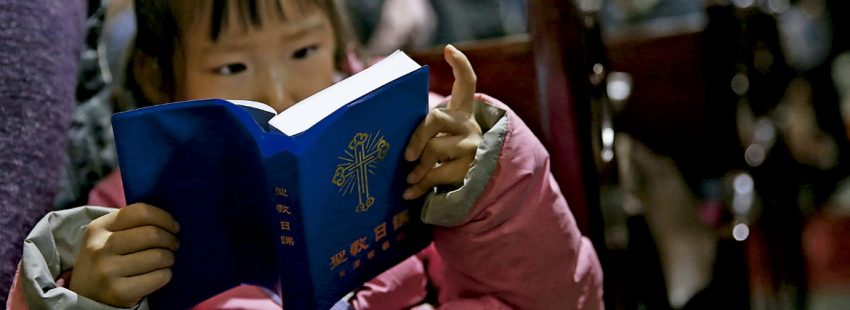 Una niña china, lee una biblia en misa