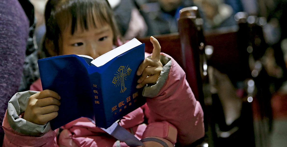 Una niña china, lee una biblia en misa