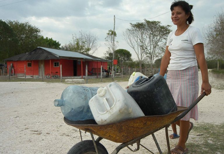 Una mujer acarrea bidones para surtirse de agua potable en una comunidad latinoamericana