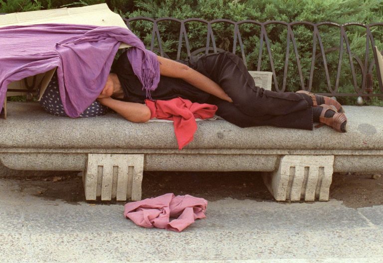 Una indigente descansa en un banco de la calle