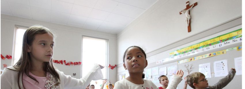 Chicos y chicas bailan en un aula con un crucifijo en la pared