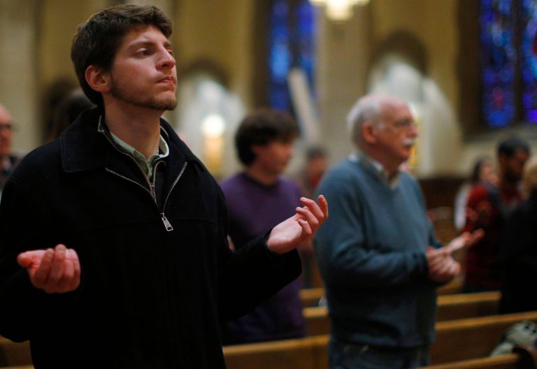 Un joven y varias personas mayores rezan en una iglesia semivacía