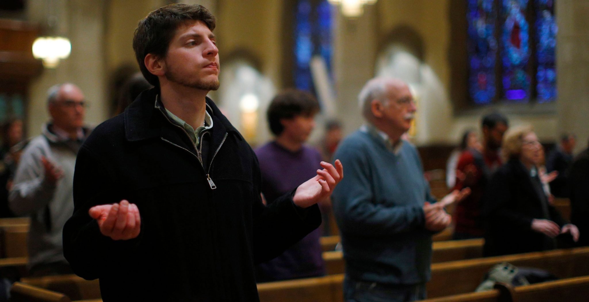 Un joven y varias personas mayores rezan en una iglesia semivacía