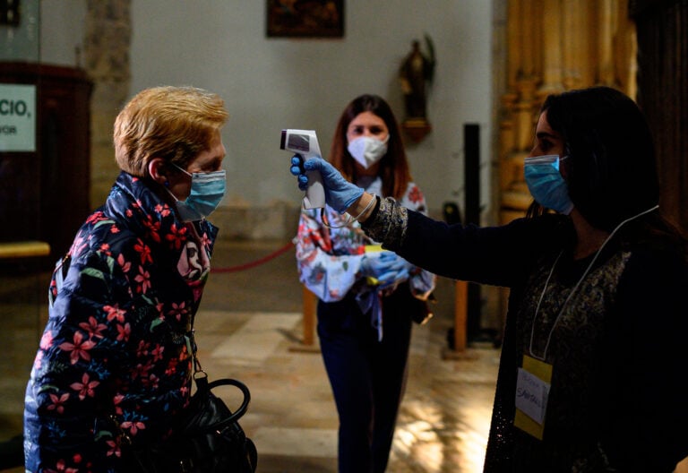Una voluntaria toma la temperatura a los fieles que acuden a misa en la catedral de Alcalá de Henares