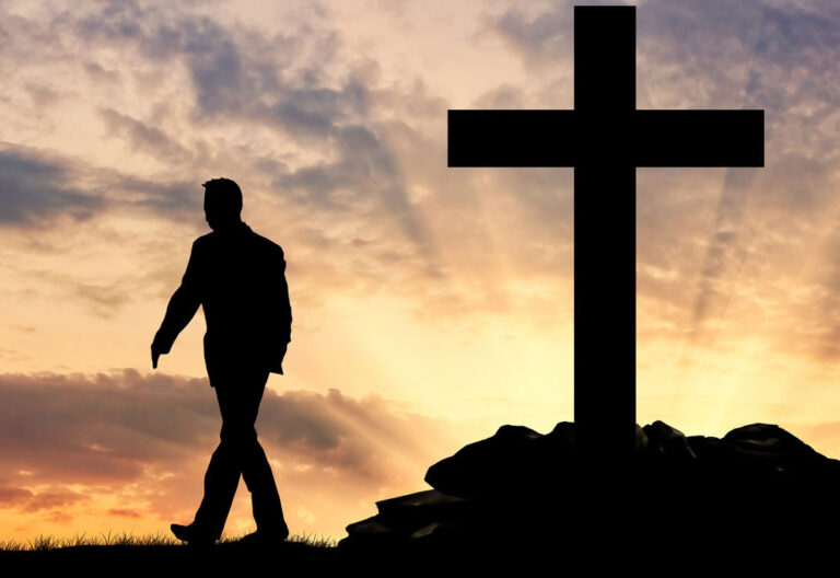 Un hombre alejándose de una gran cruz, al atardecer