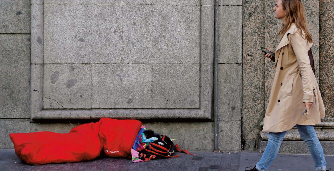 Una mujer pasa por delante de una tienda de lujo en Madrid en la que un pobre pide a la puerta