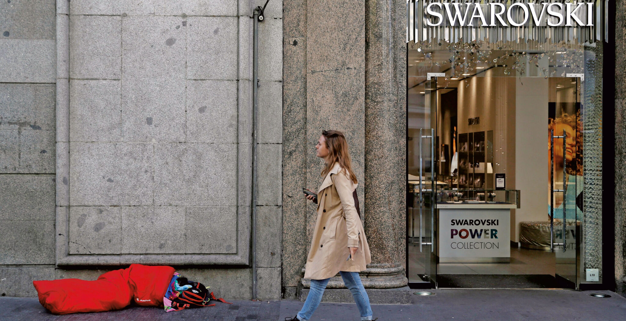 Una mujer pasa por delante de una tienda de lujo en Madrid en la que un pobre pide a la puerta