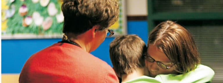 Un chico y una chica se abrazan en presencia de una mujer