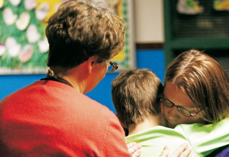 Un chico y una chica se abrazan en presencia de una mujer