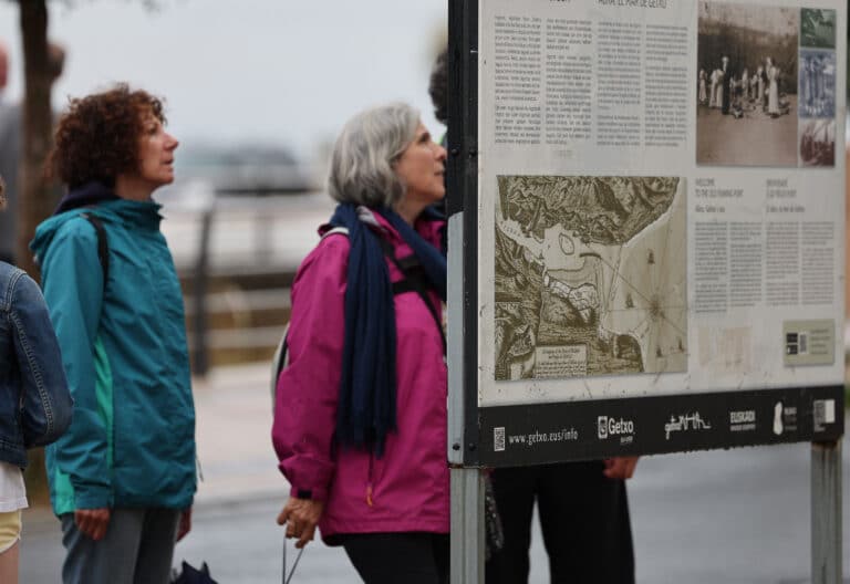 Visitantes en el País Vasco contemplan un cartel de información turística