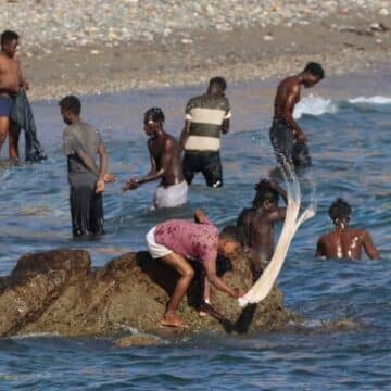 Migrantes lavan su ropa en una playa de Ceuta. Foto: Efe